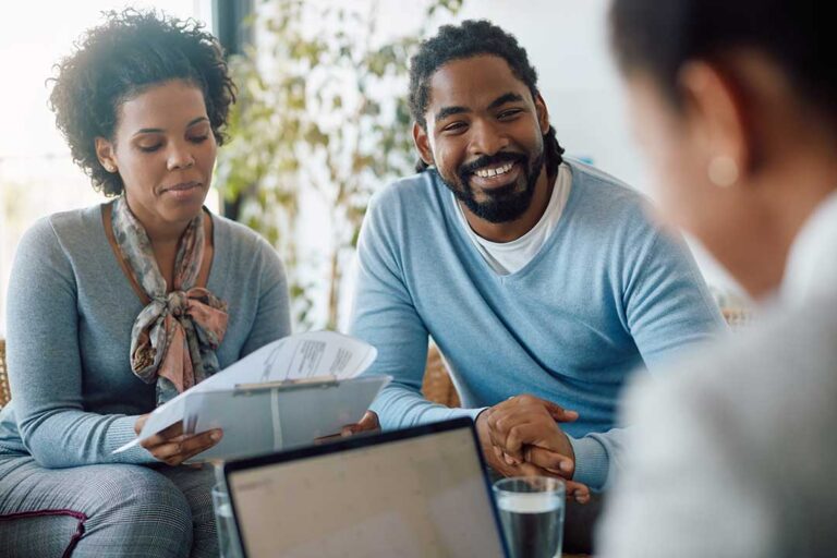 A diverse group of adults studying health insurance documents together at a kitchen table.